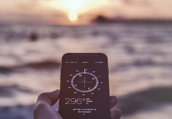 Smartphone mit Kompassanzeige vor einer entspannenden Seelandschaft bei Sonnenuntergang.