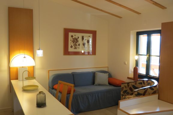 Gemütlicher Wohnraum mit Sofa, Tisch und Kunstwerk an der Wand. Helle Beleuchtung.