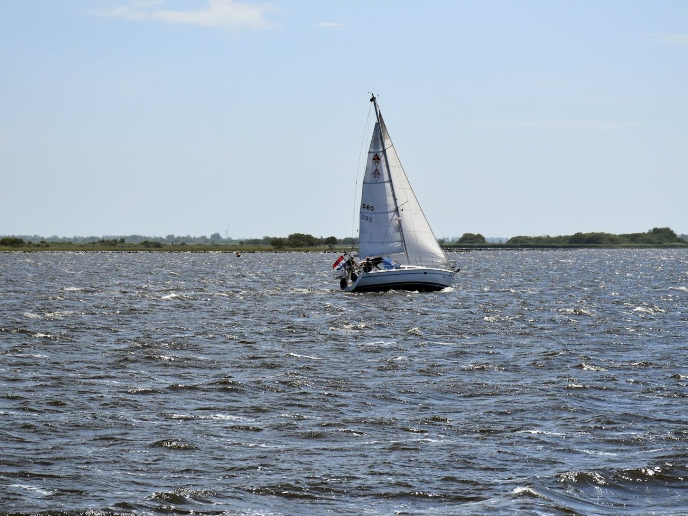 Segelboot auf einem ruhigen Gewässer, umgeben von grüner Landschaft im Hintergrund.