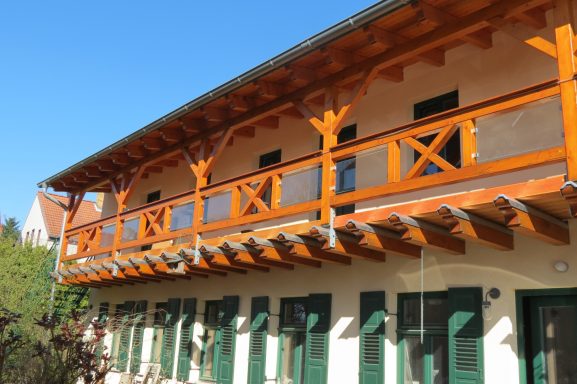 Hölzernes Obergeschoss eines Gebäudes mit Balkon und grünen Fenstern.