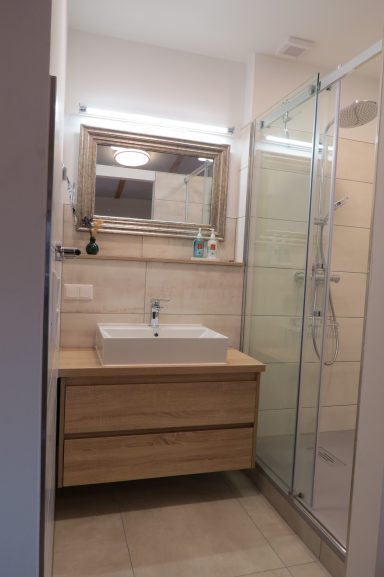 Helles Badezimmer mit Doppelwaschbecken, Spiegel und gläserner Dusche.